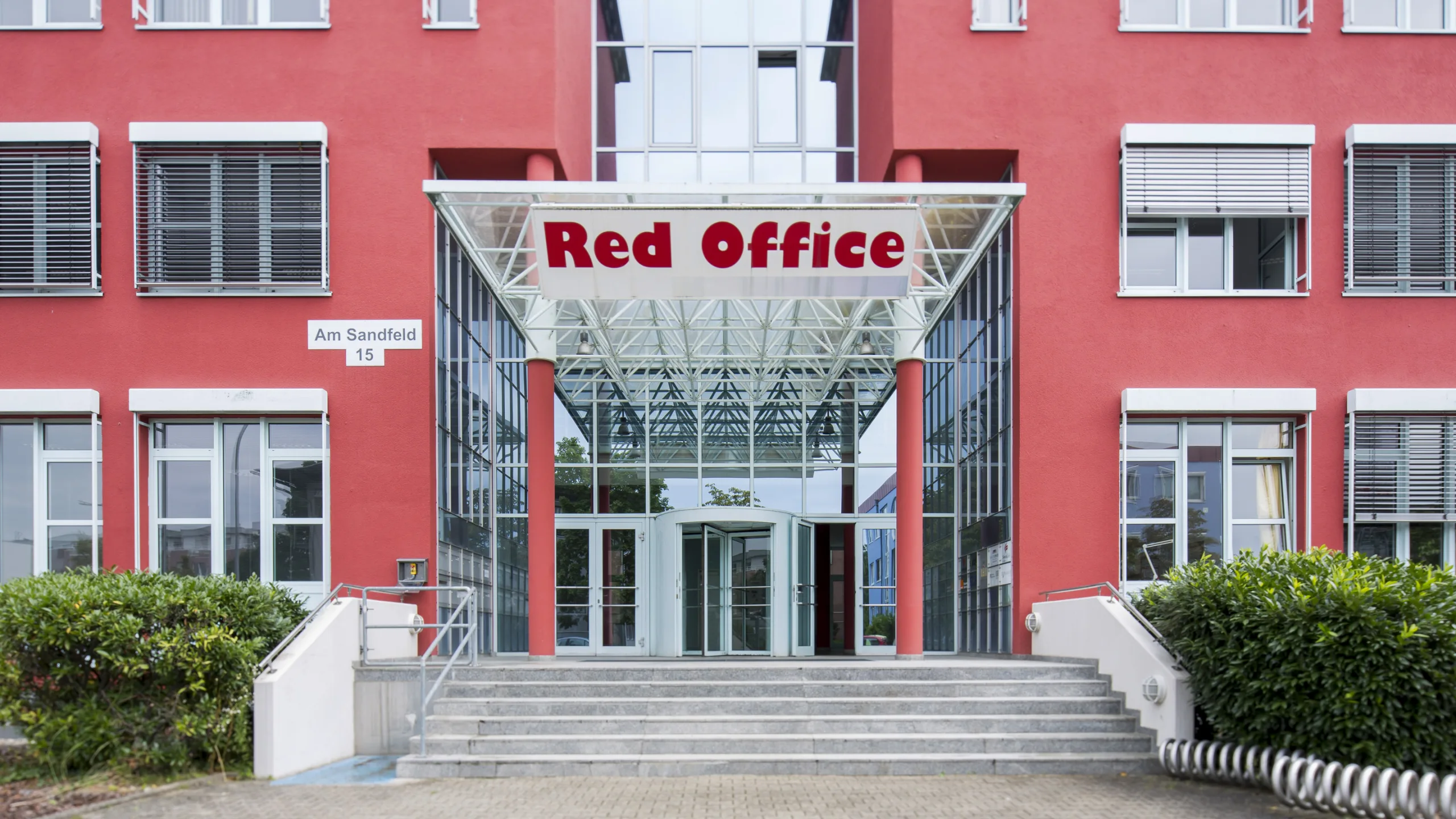 Eingang des Red Office mit gläsernem Vordach und roten Säulen